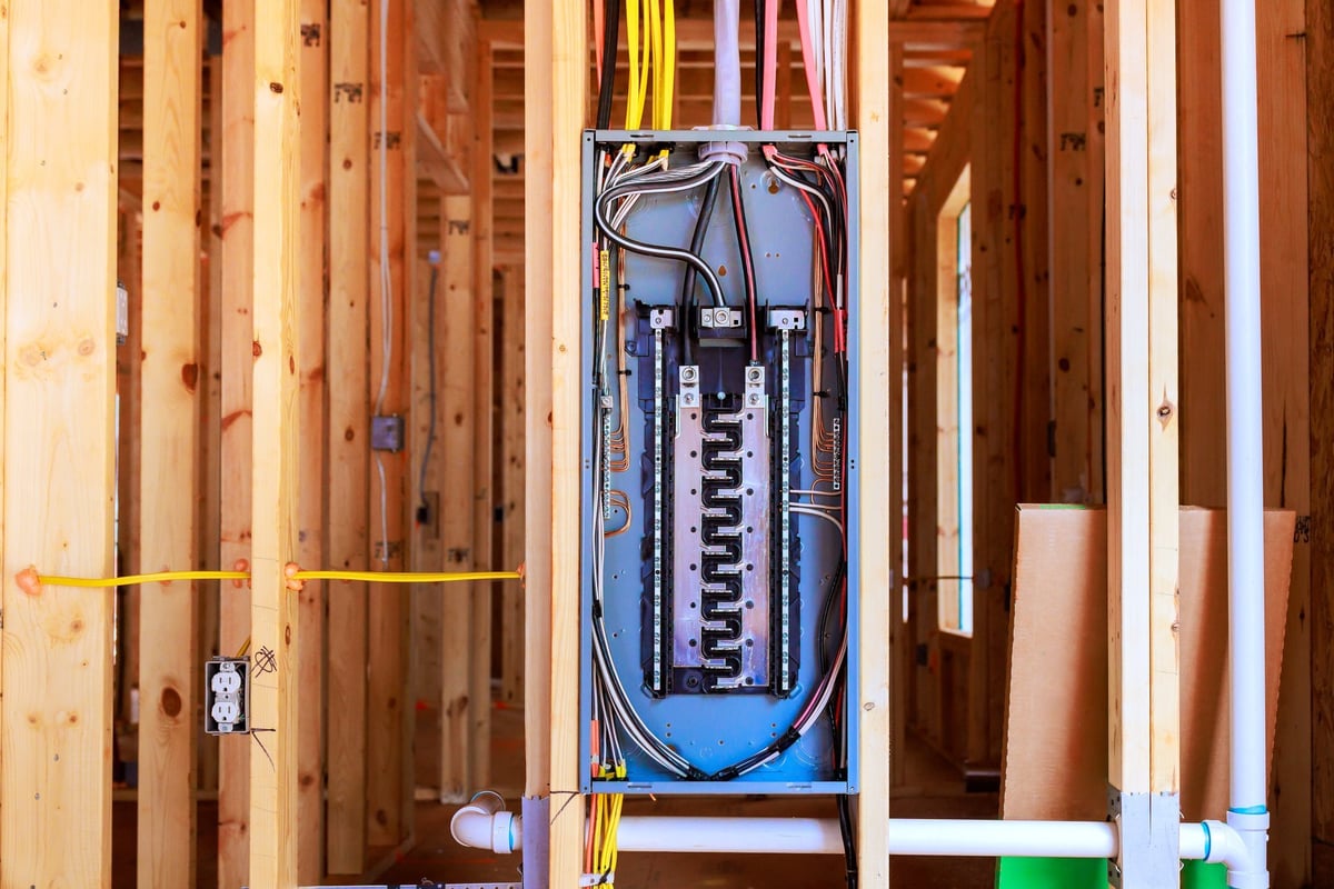 Workers install an electrical panel in newly built house with wooden framing wires in plain view.