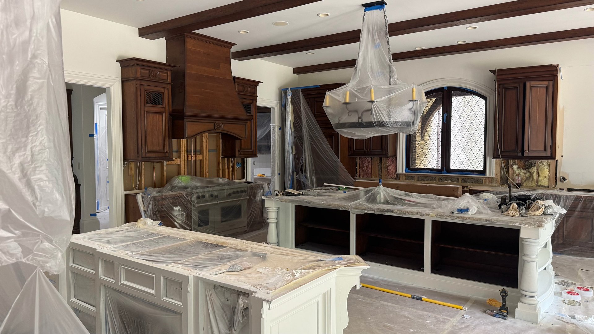 Interior of upscale kitchen under renovation with marble countertops, dark wood cabinetry, and exposed ceiling beams
