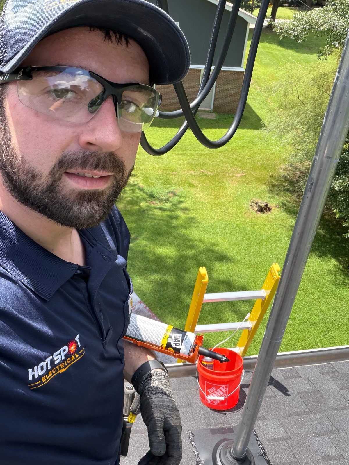 Man in safety glasses and cap holding extension ladder near house with green yard visible behind
