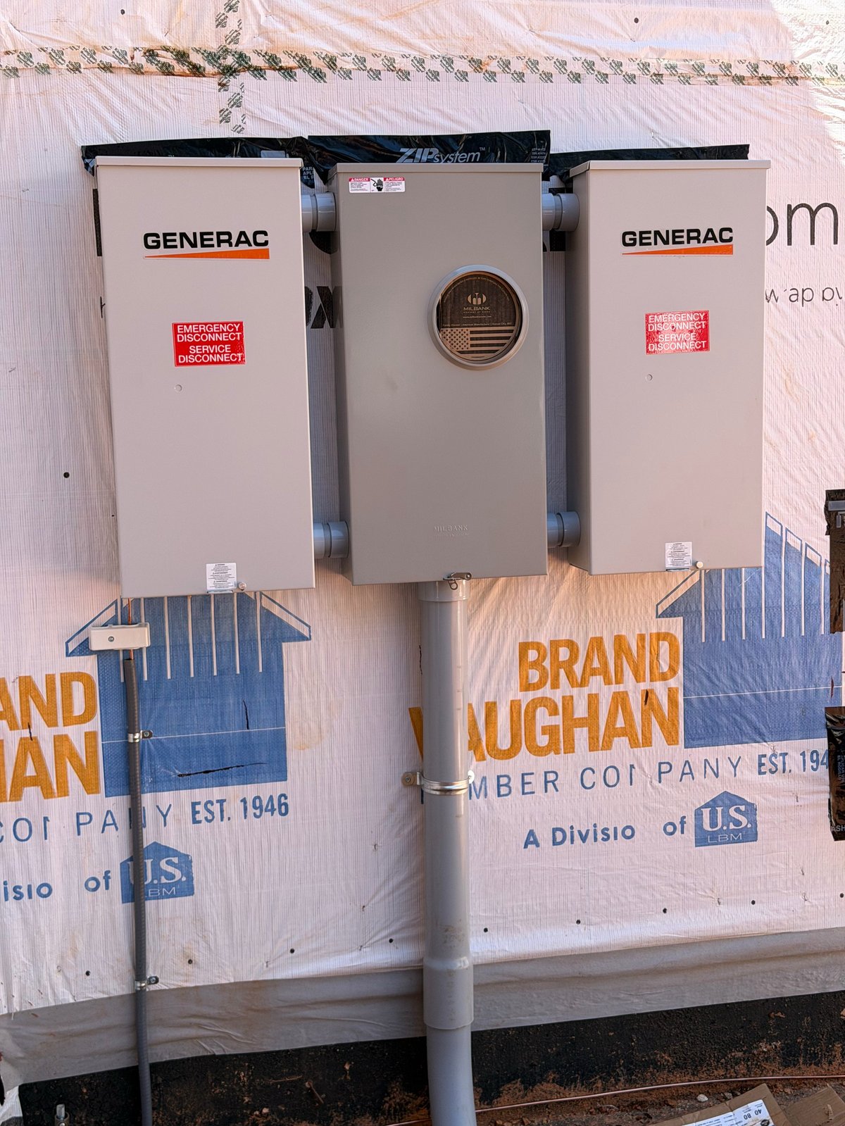 Three Generac electrical transfer switches mounted on a white wall with lumber company branding visible below