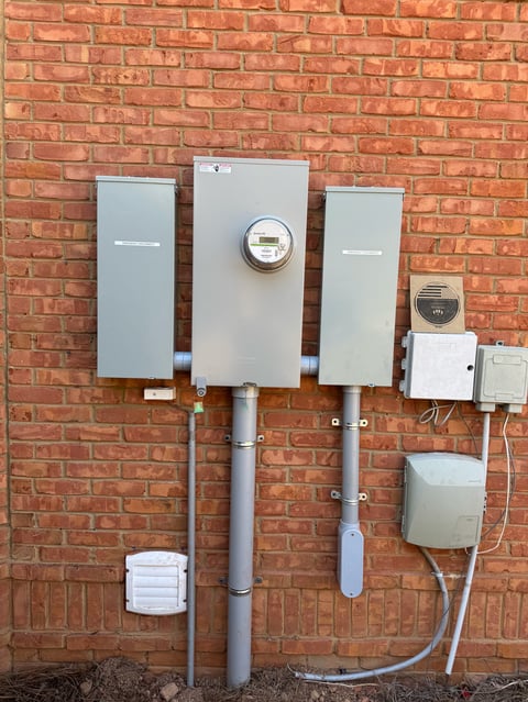 Electric meters and utility boxes mounted on a red brick wall with pipes and wiring.