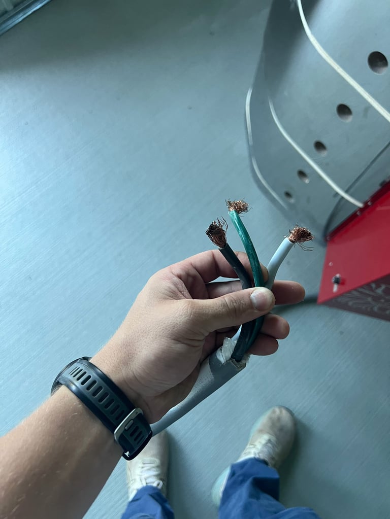 Hand holding three exposed copper electrical wires with stripped ends against a blue metal surface