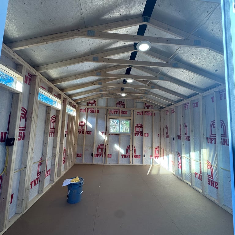 Interior of a metal shipping container with insulation, exposed beams, ceiling fans, and a blue bucket on the floor