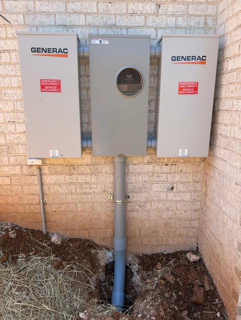 Three Generac electrical panels mounted on a brick wall with PVC conduit running to the ground
