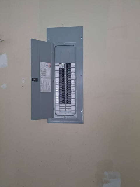 Open gray electrical panel box mounted on wall showing circuit breakers and wiring diagram