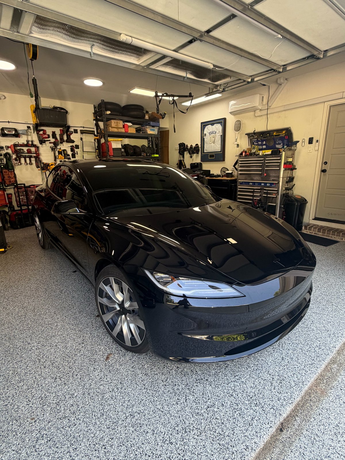 Black Tesla electric car in a well-equipped garage workshop with tools and storage
