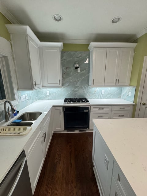 Modern kitchen with white cabinetry, marble backsplash, black gas range, and green accent walls