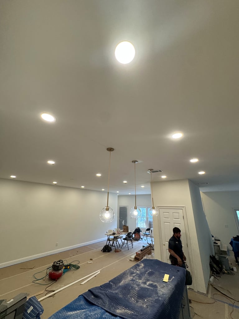 Interior of a room under renovation with recessed ceiling lights, drop cloths, and construction equipment visible.
