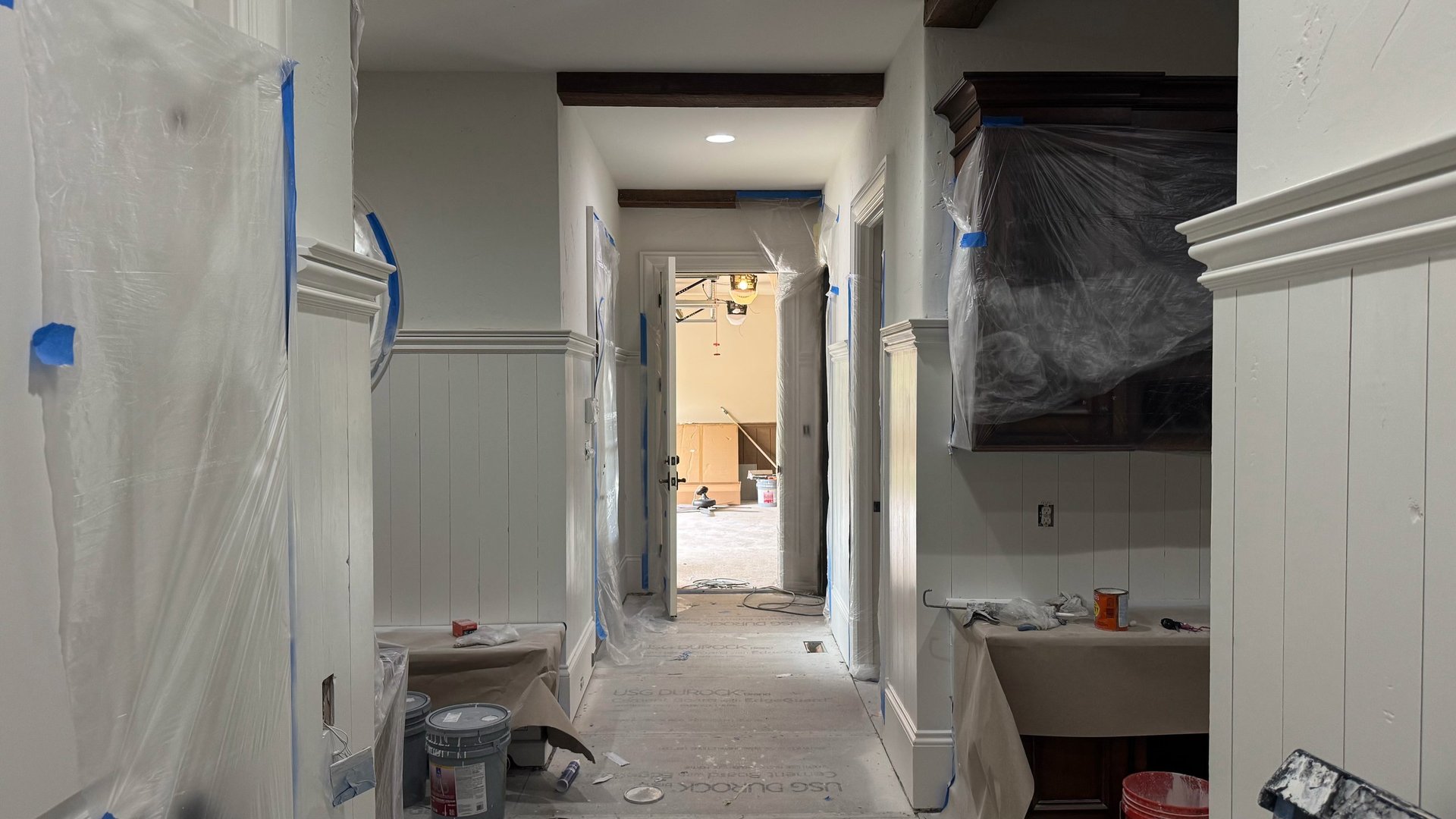 Empty hallway with white drywall, plastic sheeting, and construction materials during home renovation