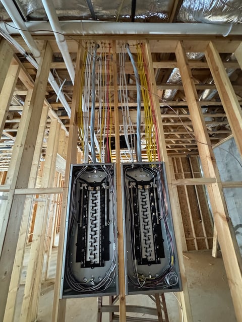 Two black electrical panels mounted in wooden wall framing with conduit running above during home construction