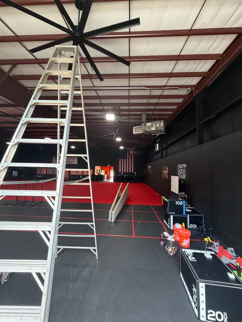 Interior warehouse space with white aluminum ladder against exposed beam ceiling and large black ceiling fan