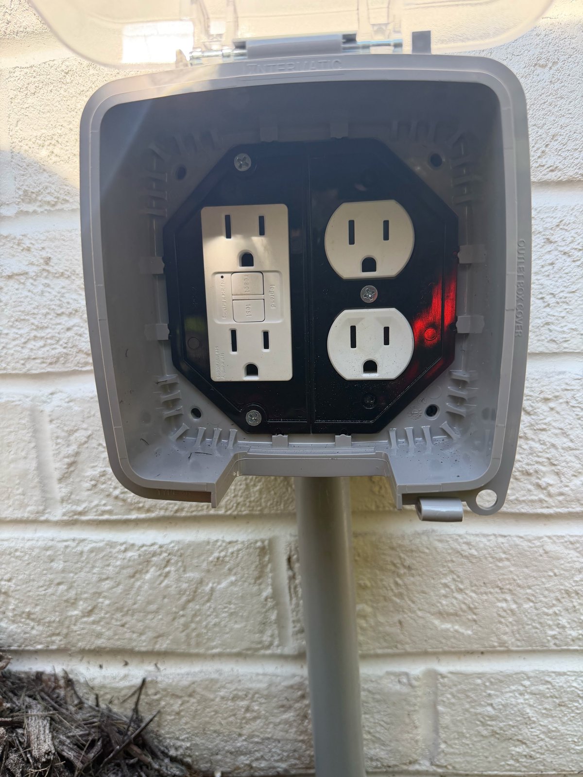 Exterior electrical outlet box mounted on white brick wall with two outlets and a switch installed