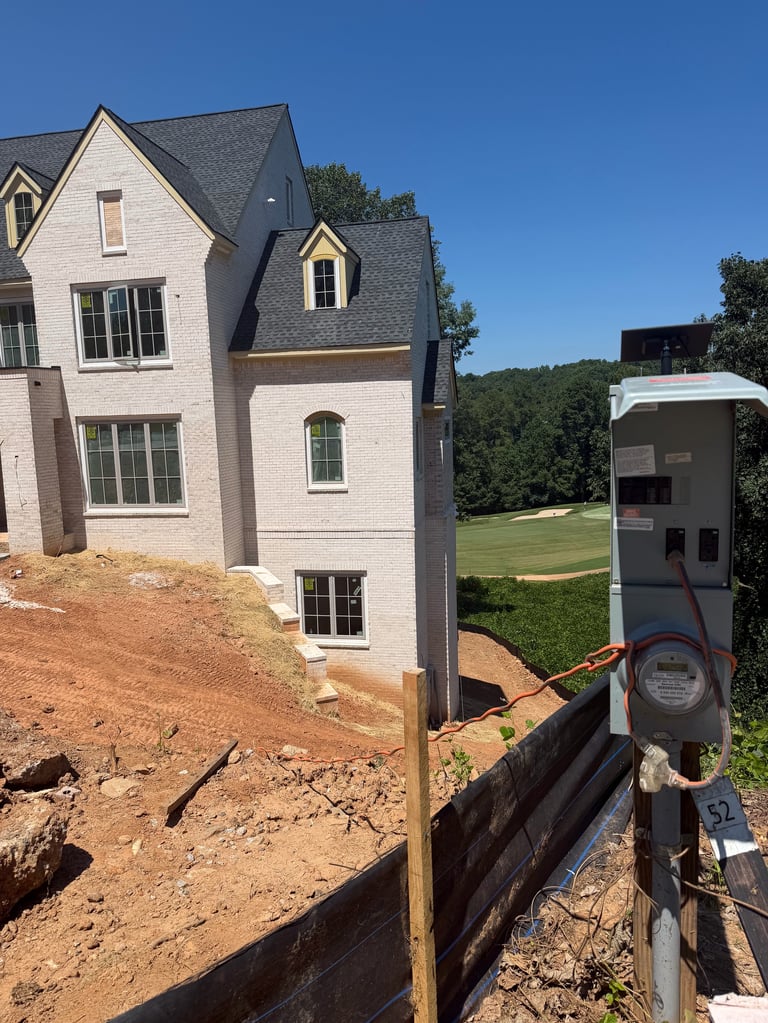 New residential home under construction with brick exterior, electrical meter visible in foreground, clear blue sky and green lawn in background