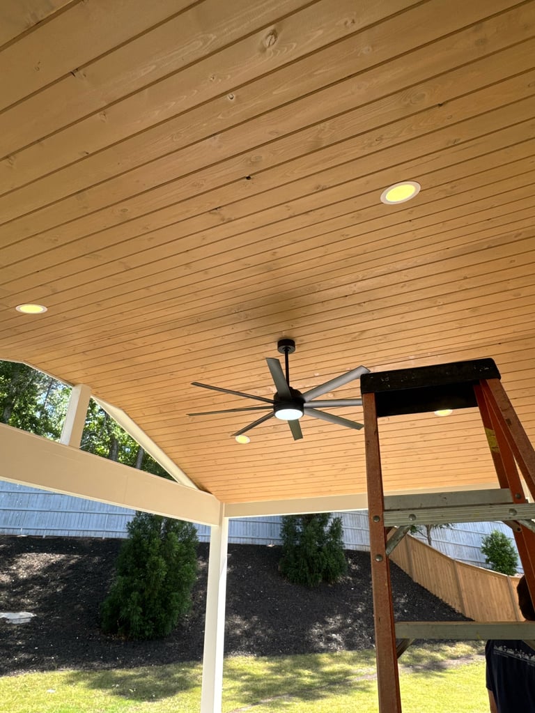 Modern ceiling fan and recessed lighting mounted on wooden slat ceiling in covered outdoor patio area